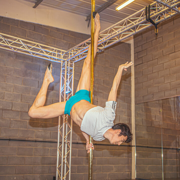 Male pole dancer on brass pole in a pole dance studio